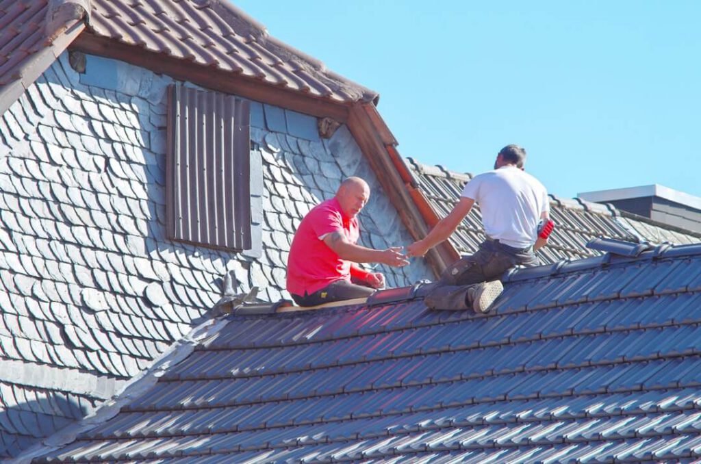 Two roofers sitting on a roof handing each other tools